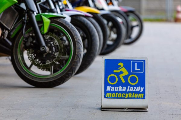 Na pierwszym planie znak nauki jazdy motocyklem. W tle motocykle w szeregu